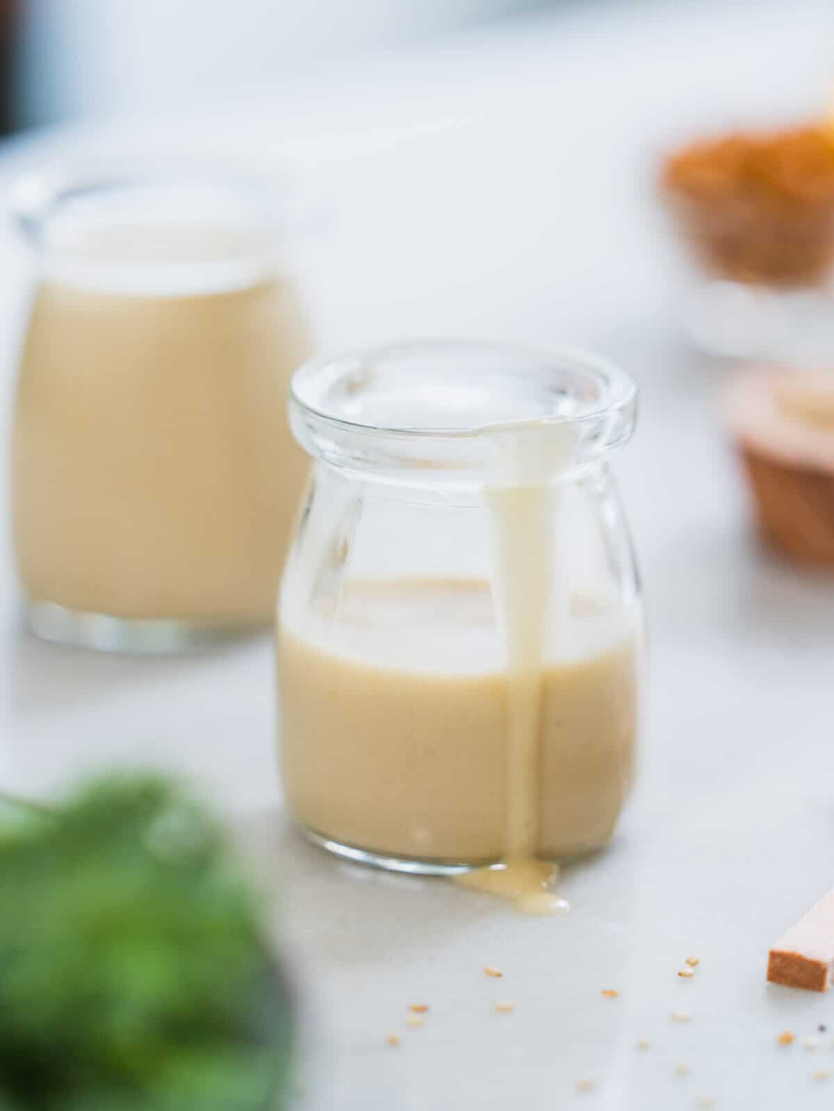 maple tahini dressing in a glass recipient dripping sauce in a table.