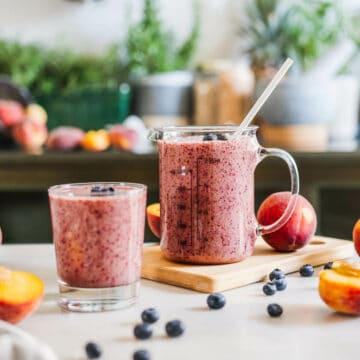peach blueberry smoothie without yogurt or banana served in two glasses with peaches and blueberries on the table.