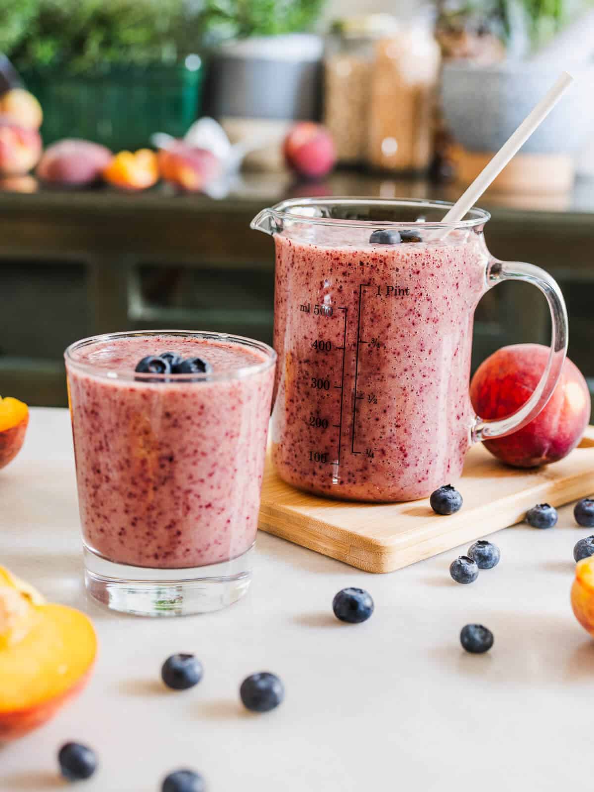 peach blueberry smoothie without yogurt or banana served in two glasses with peaches and blueberries on the table.