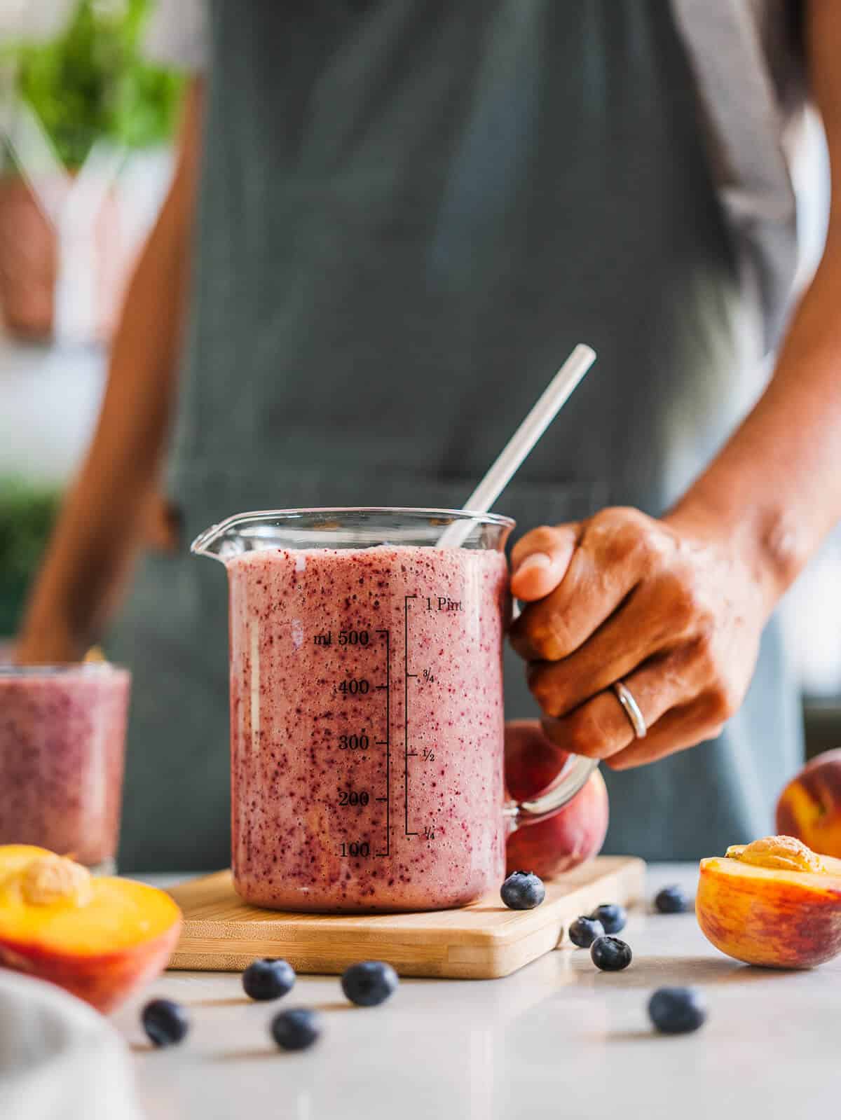 man holding a glass glass with peach blueberry smoothie served.