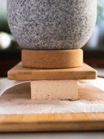 pressing tofu between paper towels with a heavy mortar on top.