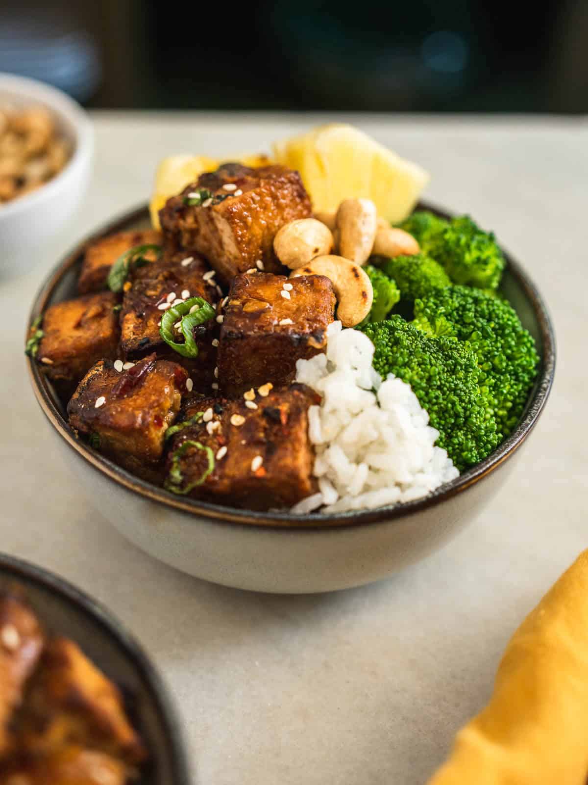 crispy teriyaki toffu puffs served in bowl with broccoli, cashews, rice, and pineapple chunks.