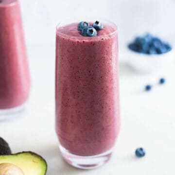 two long glasses of avocado banana blueberry smoothie with spinach.