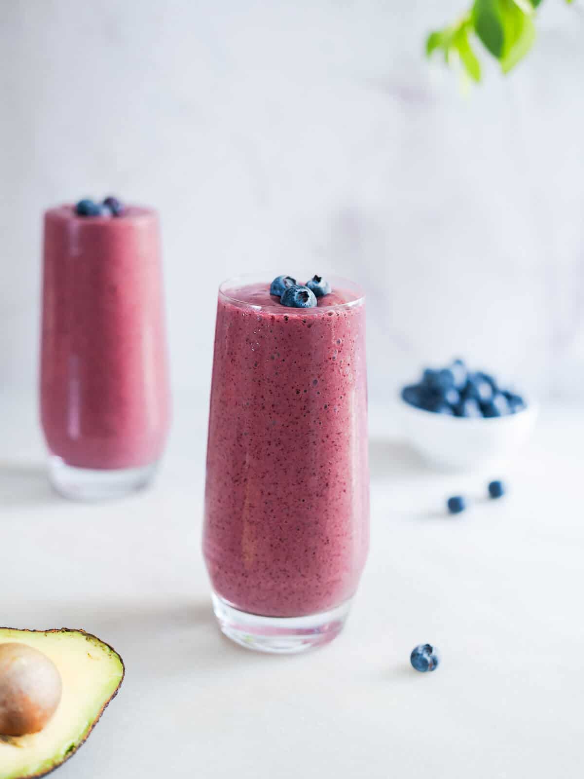 two long glasses of avocado blueberry smoothie.