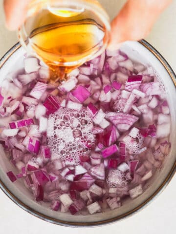 adding vinegar to a bowl with chopped red onion soaking in water.