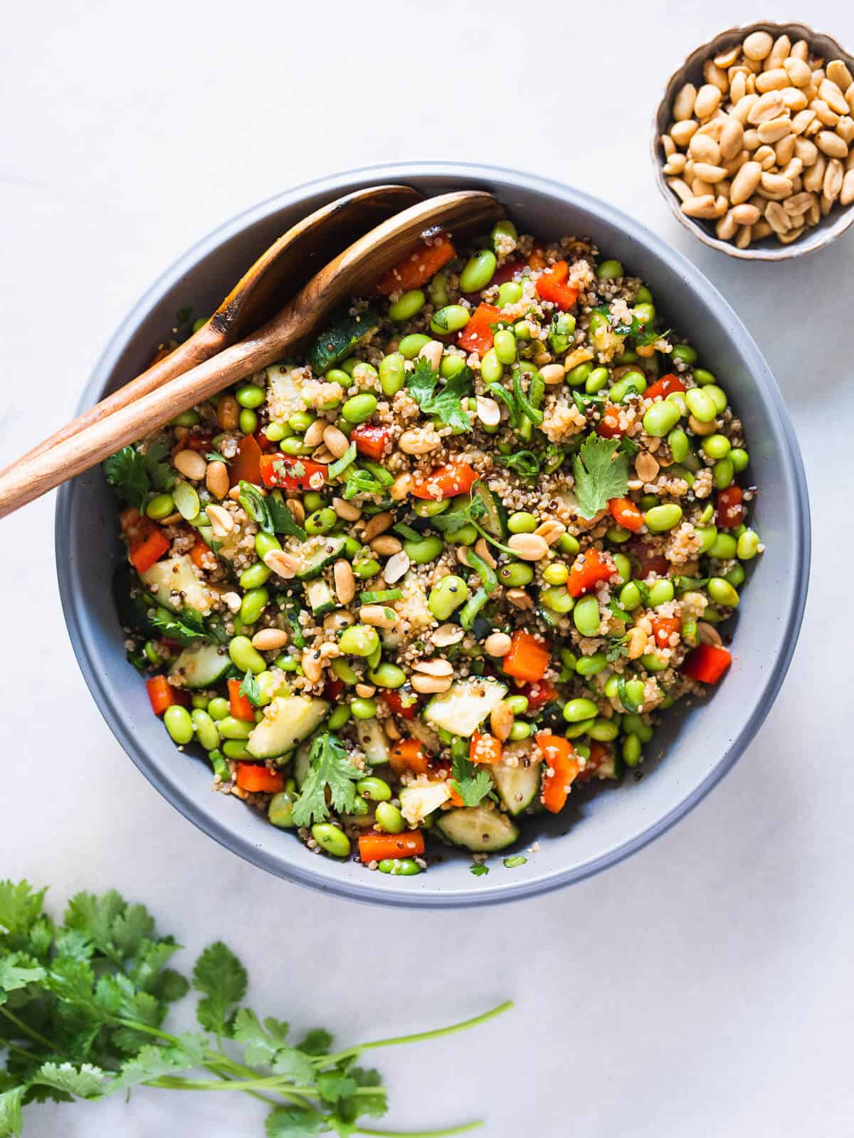 quinoa edamame salad with asian salad dressing served in a large bowl with two wooden serving spoons.