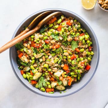quinoa edamame salad with asian salad dressing served in a large bowl with two wooden serving spoons.