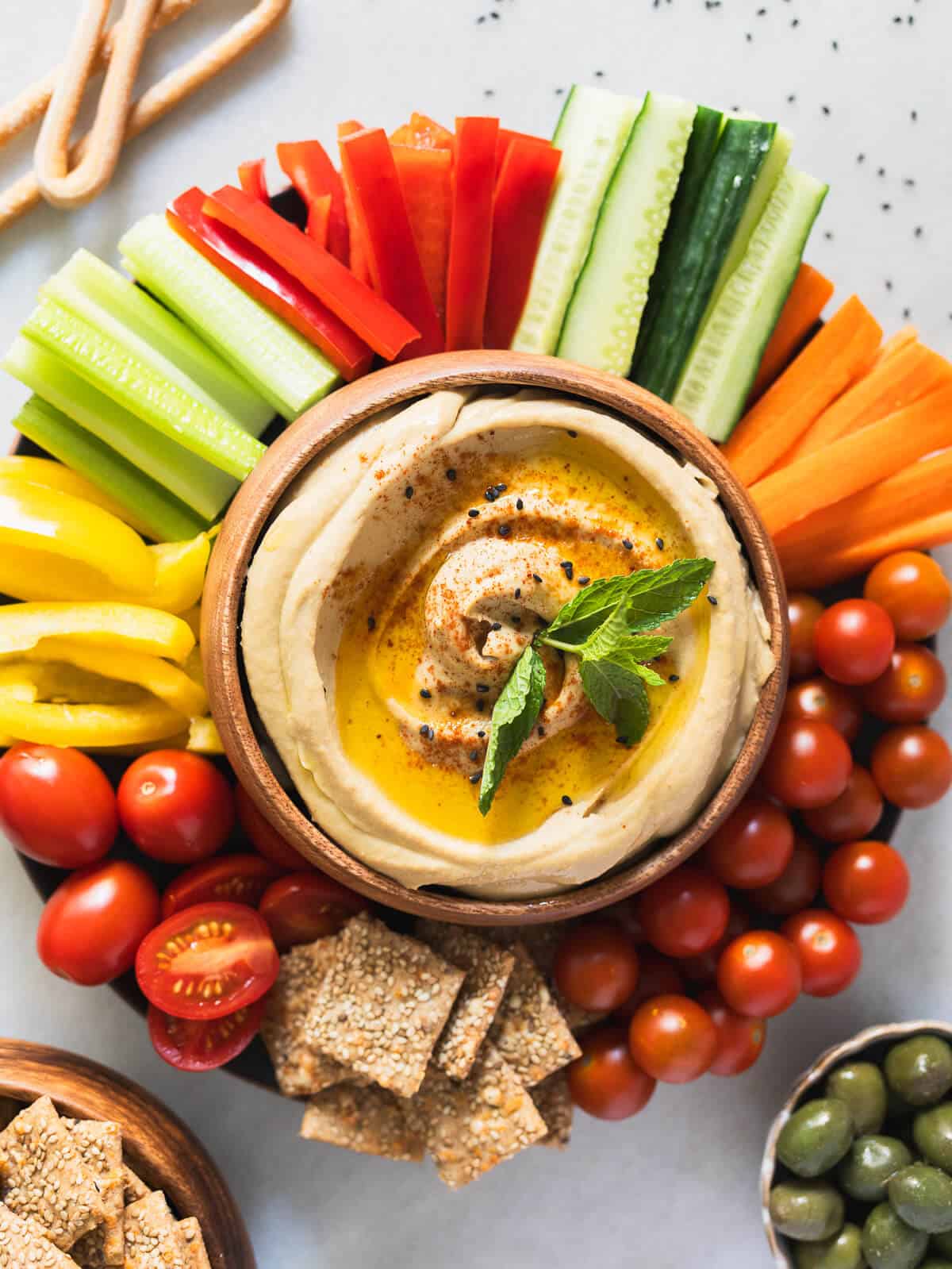 wondering what to eat with hummus? Here is a serving plate with tons of vegetables , cracker and more options with a hummus bowl in the center.