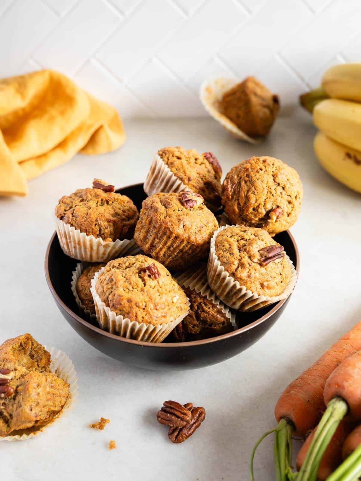 bowl of banana carrot muffins with fresh bananas and carrots.