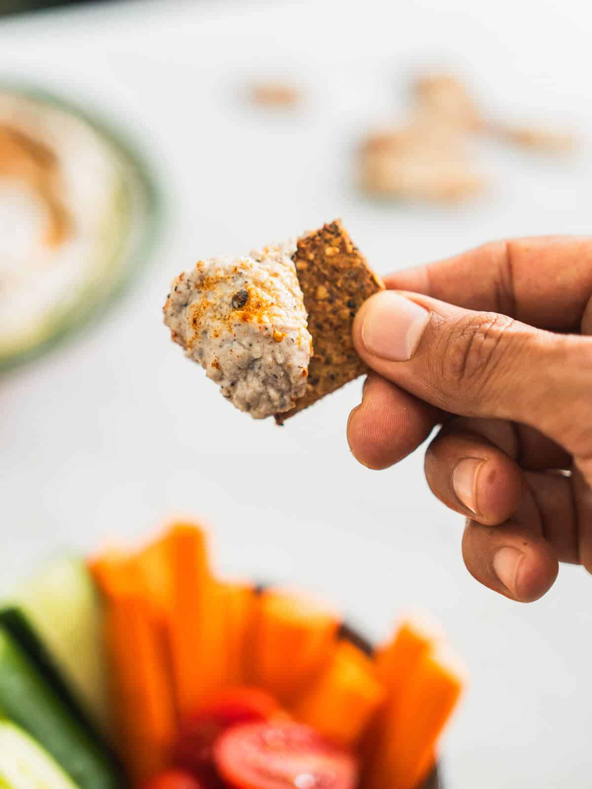 hand holding a cracker whipped with black-eye peas hummus.