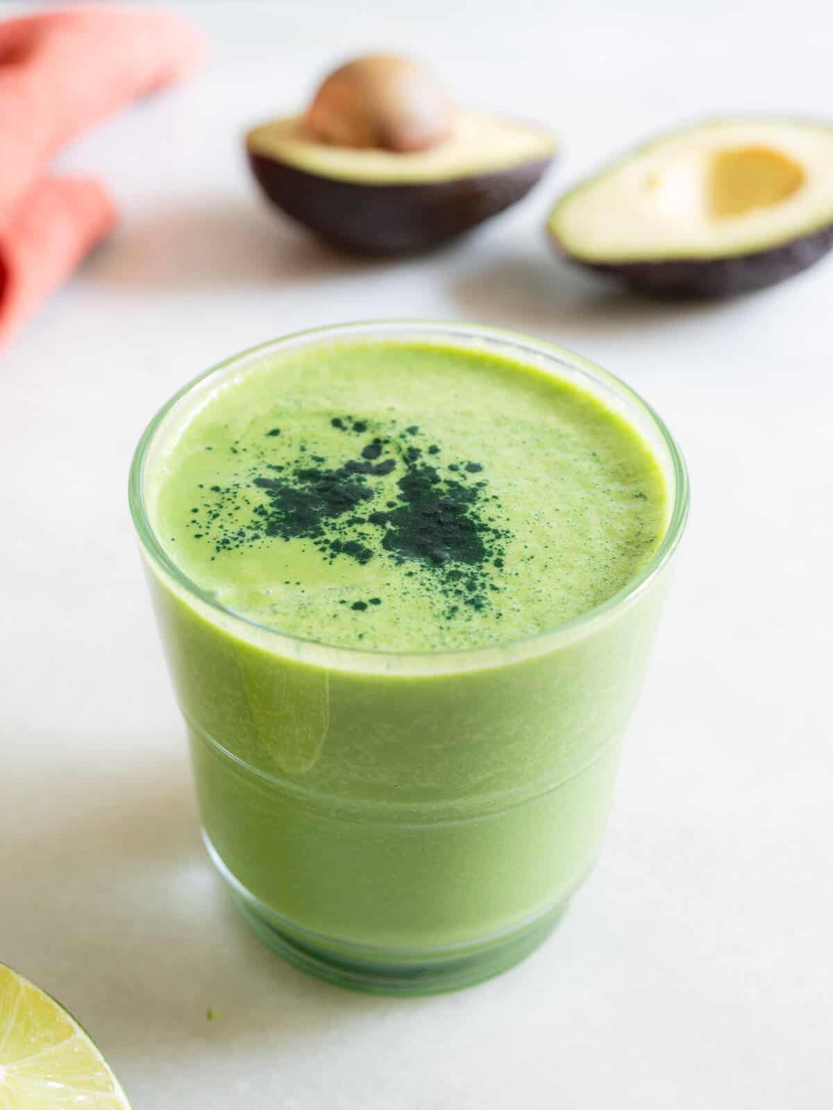 two glasses of green smoothie with avocado, and ripe fresh avocados.