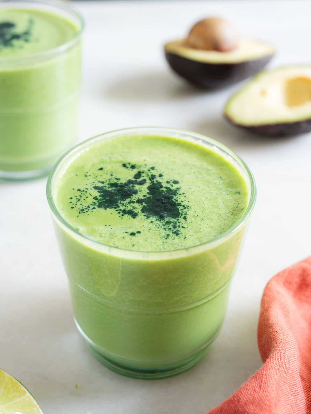 two glasses of green smoothie with avocado, and ripe fresh avocados.