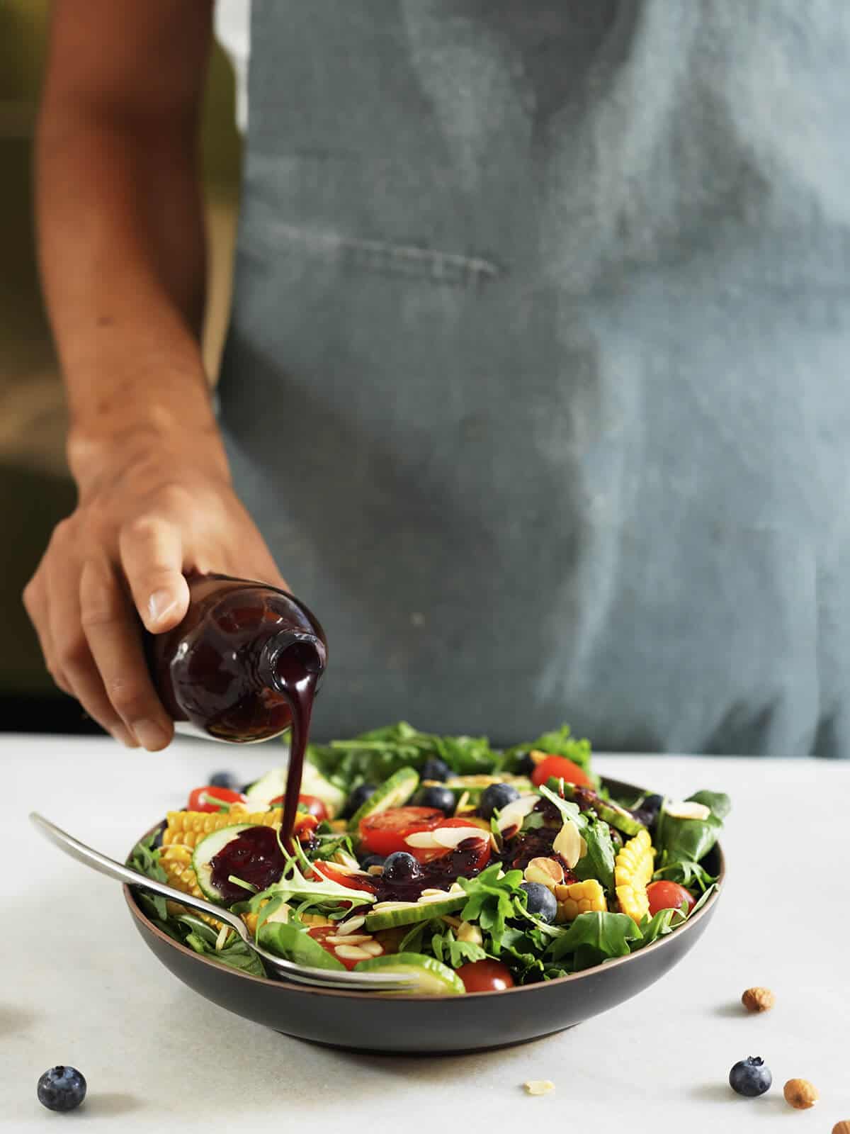 pouring blueberry dressing into spinach arugula salad.