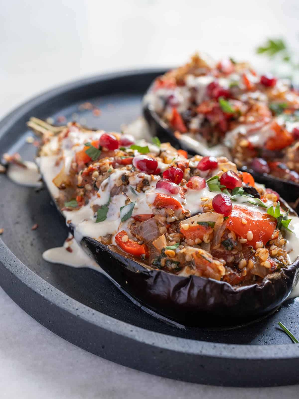 vegan stuffed eggplants served in a plate with tahini sauce, pomegranate seeds, and fresh parsley.