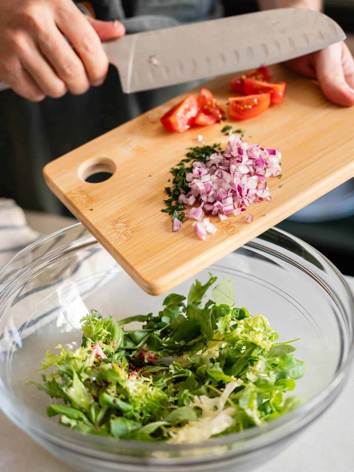 adding all the chopped veggies to the bowl of mixed greens.