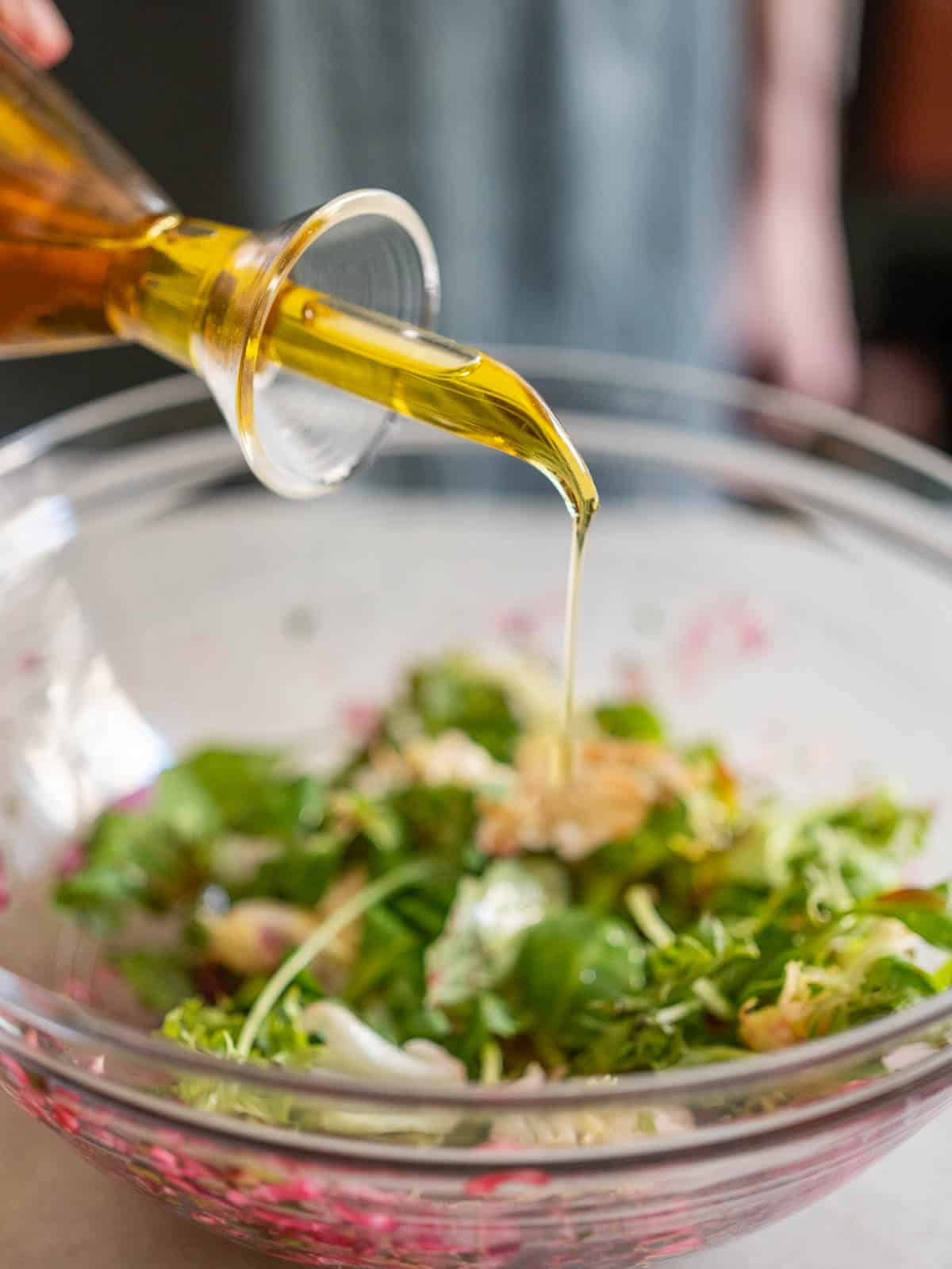 adding olive oil to the greens bowl.