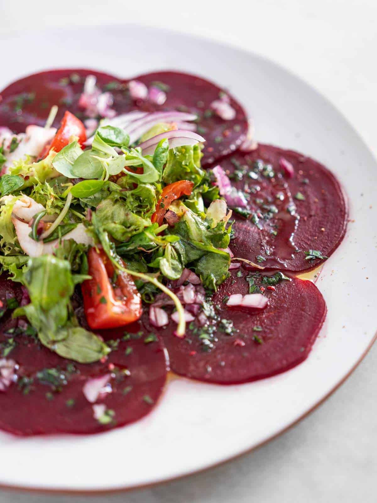 assemble the carpaccio of beets salad by laying the greens and tomatoes on top of the beets discs. 