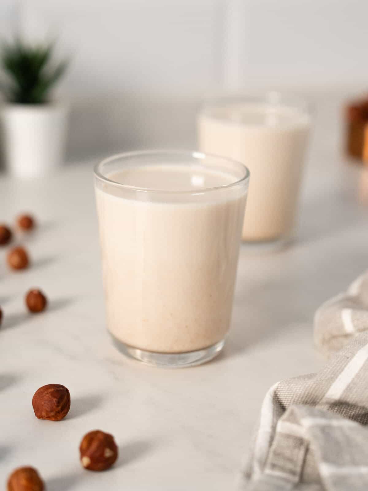 A glass of hazelnut milk with a bowl of hazelnuts beside it.