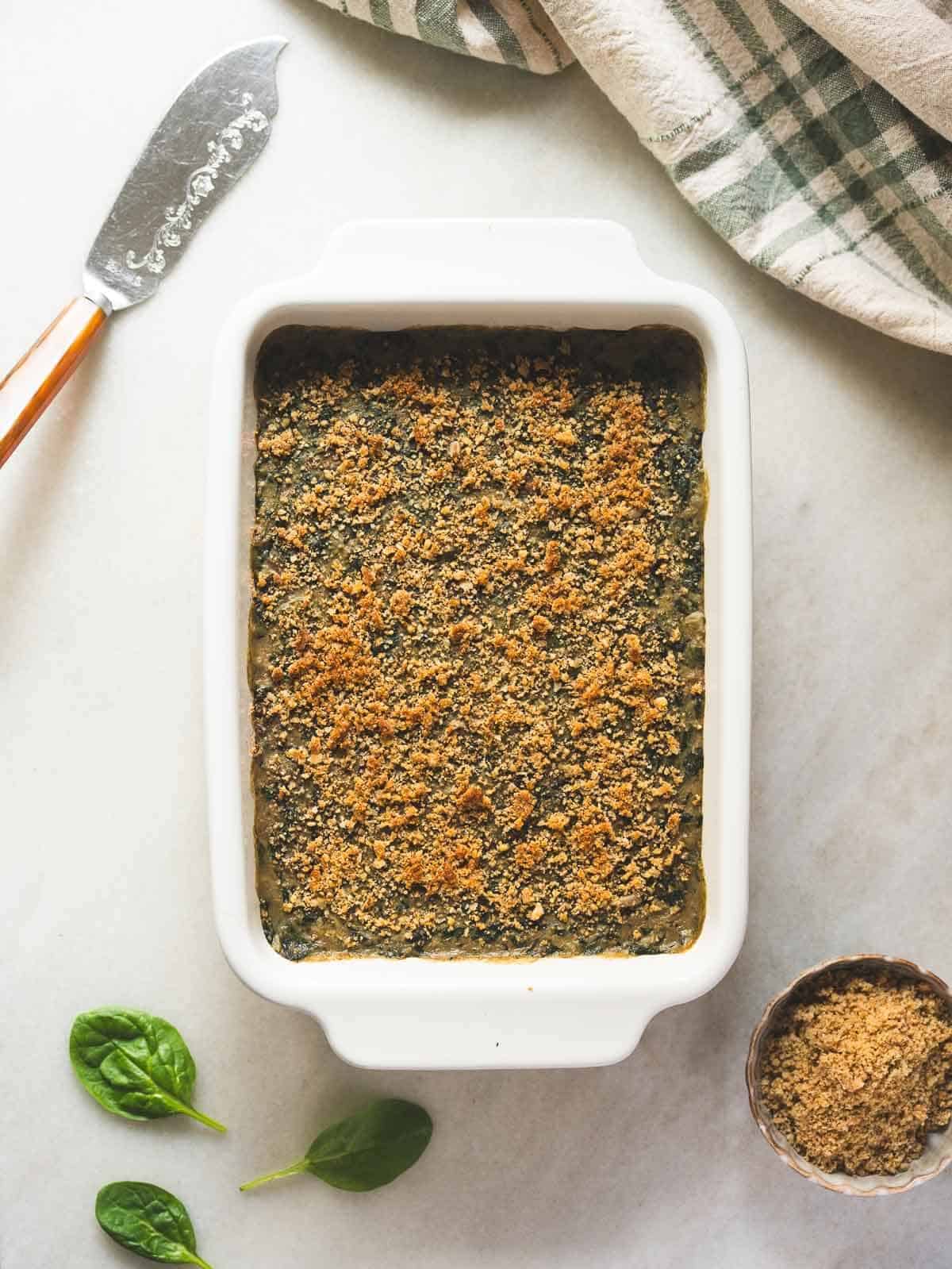 cheesy creamed spinach served on a table with a bowl containing vegan parmesan cheese.