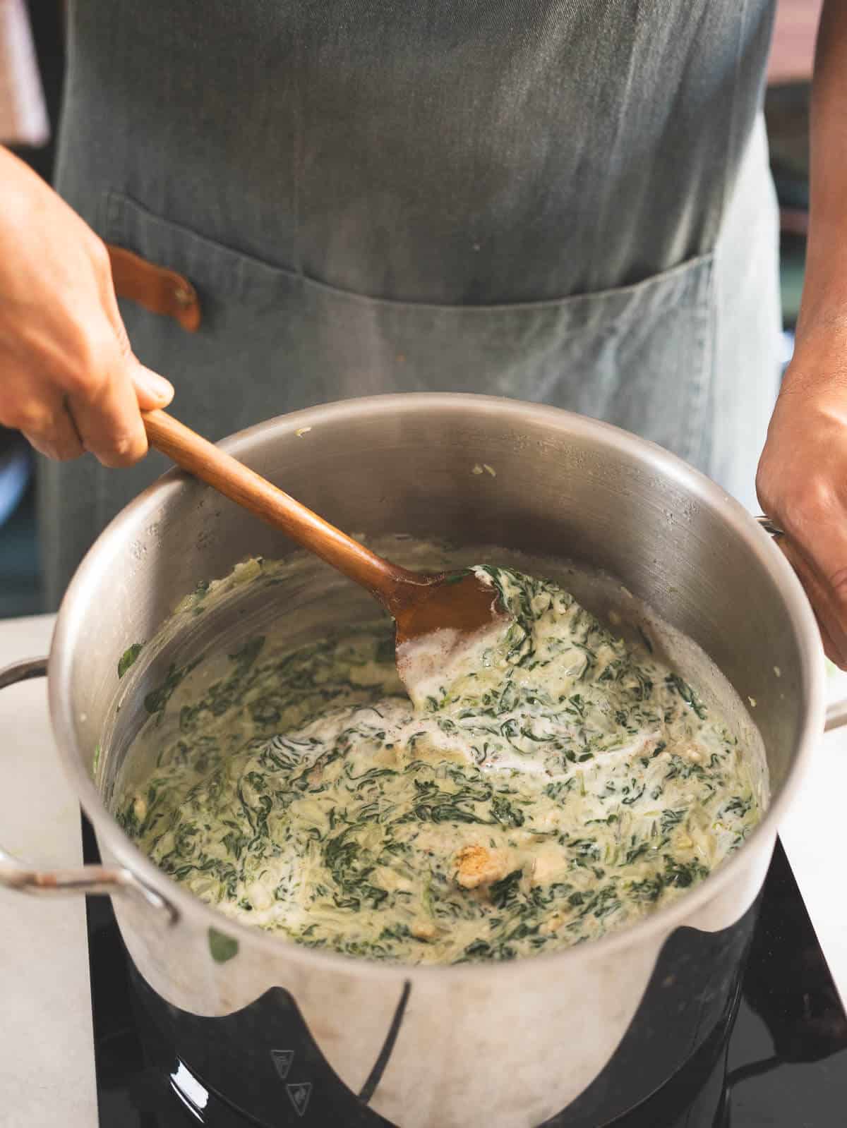 stirring creamed spinach with w wooden spoon.
