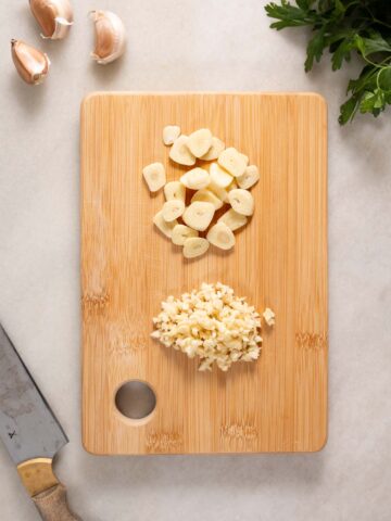 chopped garlic and sliced garlic on a wooden chopping board.