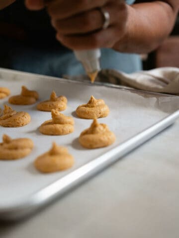 making cookies with piping bag in baking sheet.