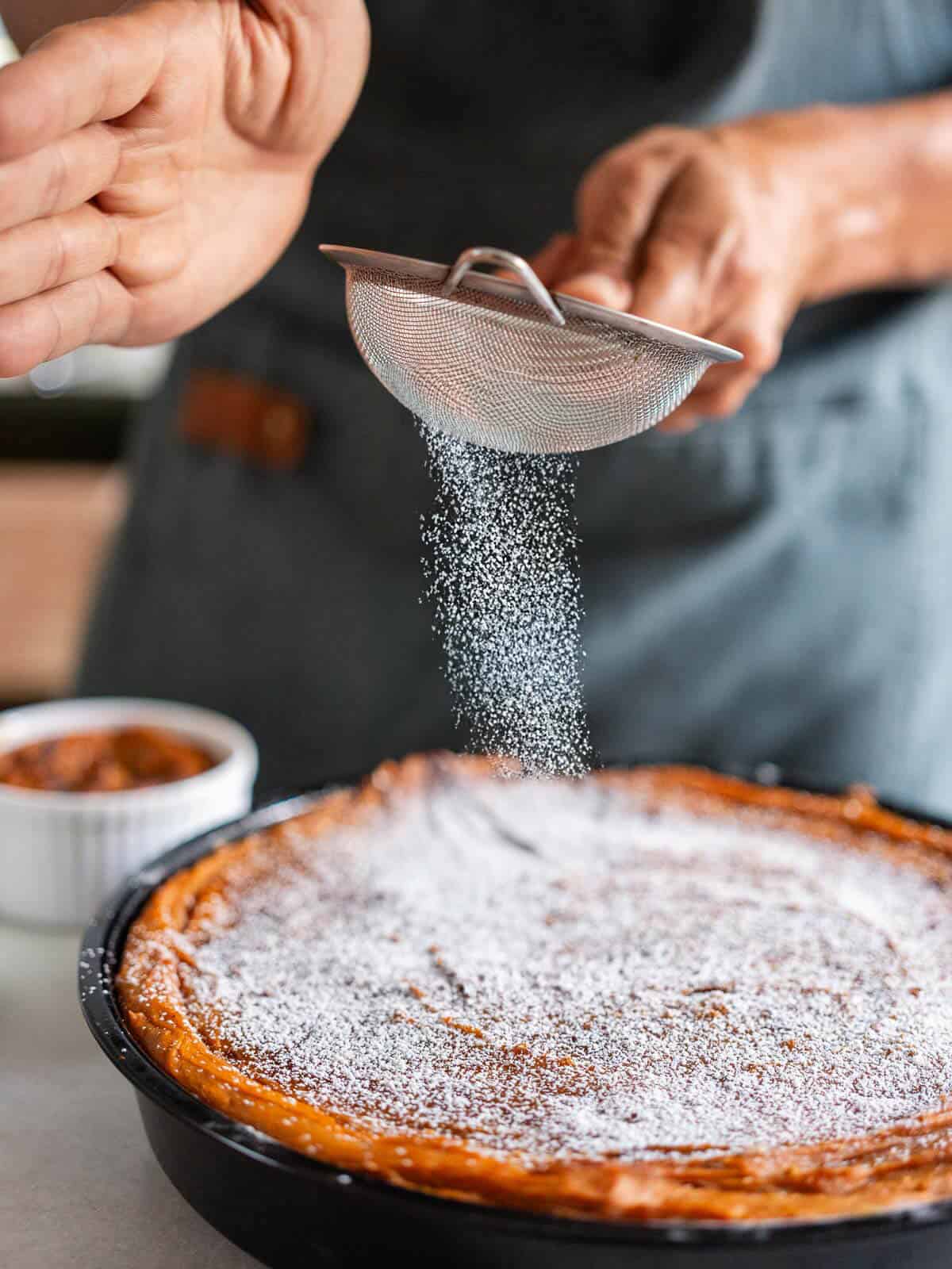 adding powdered sugar on top of the sweet potato pudding.