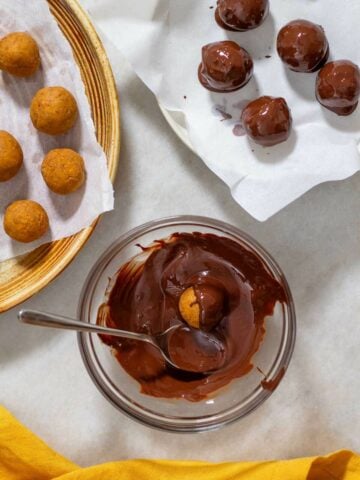 covering pumpkin protein balls with chocolate using a spoon.