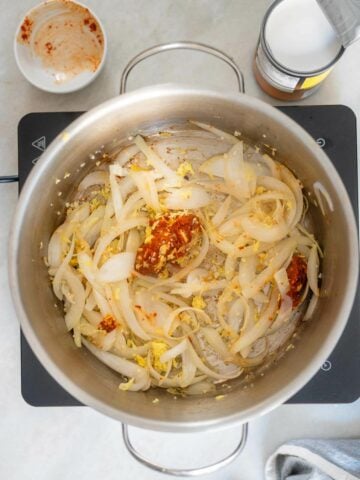 large saucepan with chopped onions, minced ginger, garlic, and red curry paste.