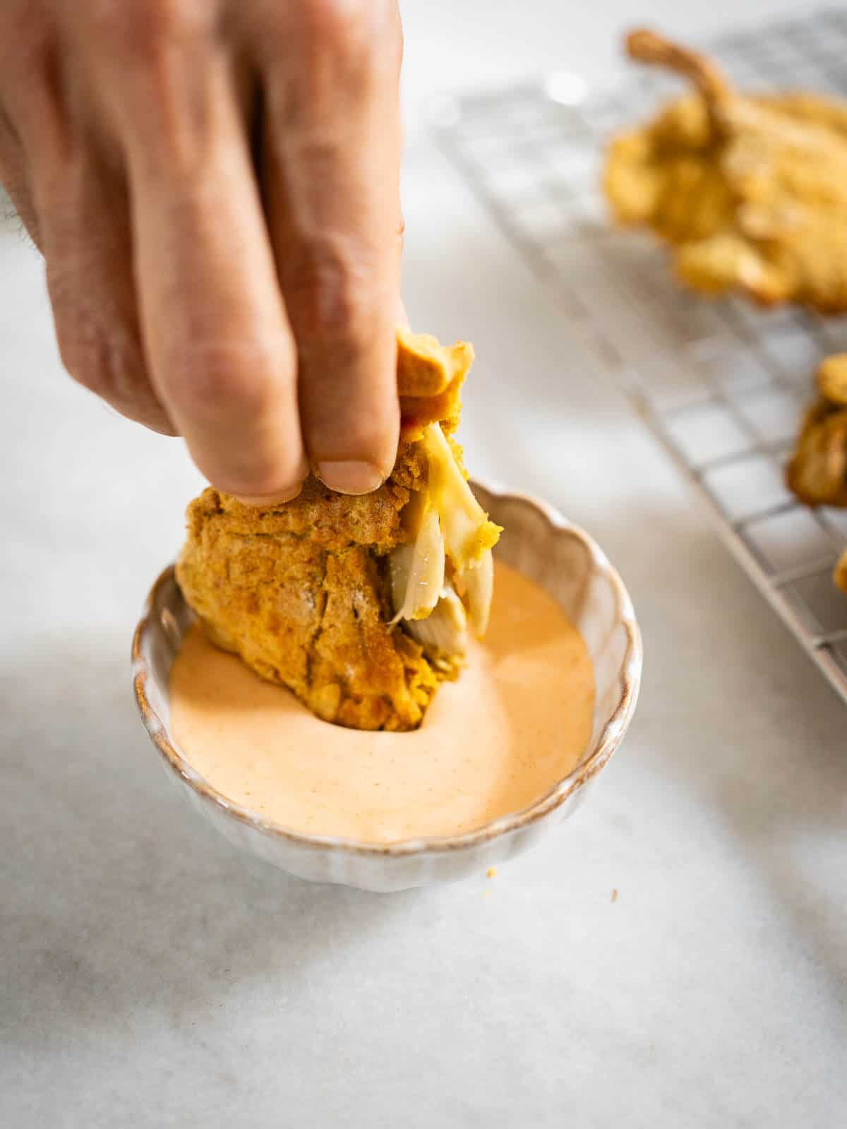 dipping a baked piece of crunchy oyster mushrooms in a mayo-sriracha dipping sauce.