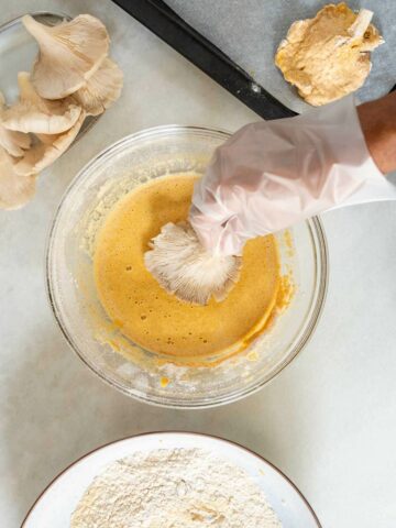 coating an oyster mushroom with batter, using a kitchen glove.
