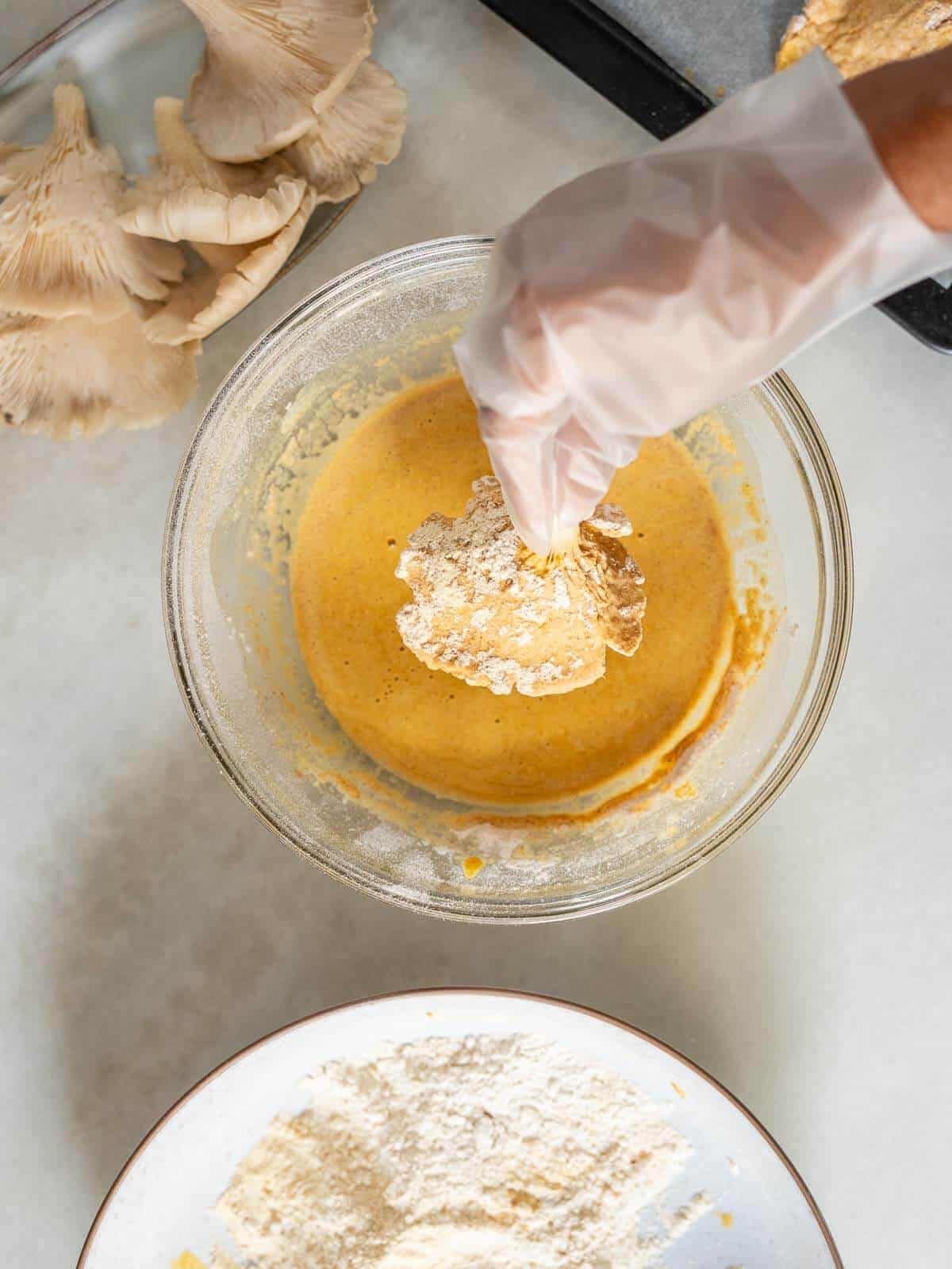 coating an oyster mushroom with batter, for the second time, using a kitchen glove.