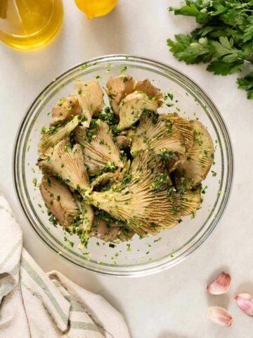 glass bowl with oyster mushrooms mixed with olive oil, salt, chopped parsley, and garlic.