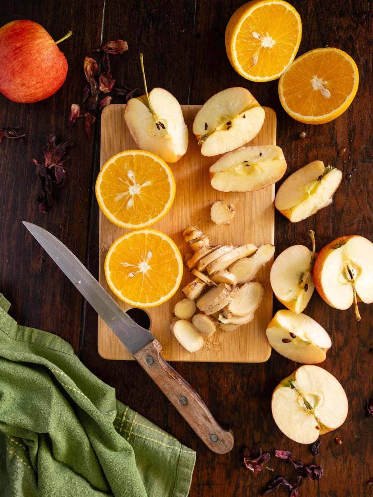 halved oranges, quartered apples, and sliced fresh ginger on a wooden table.