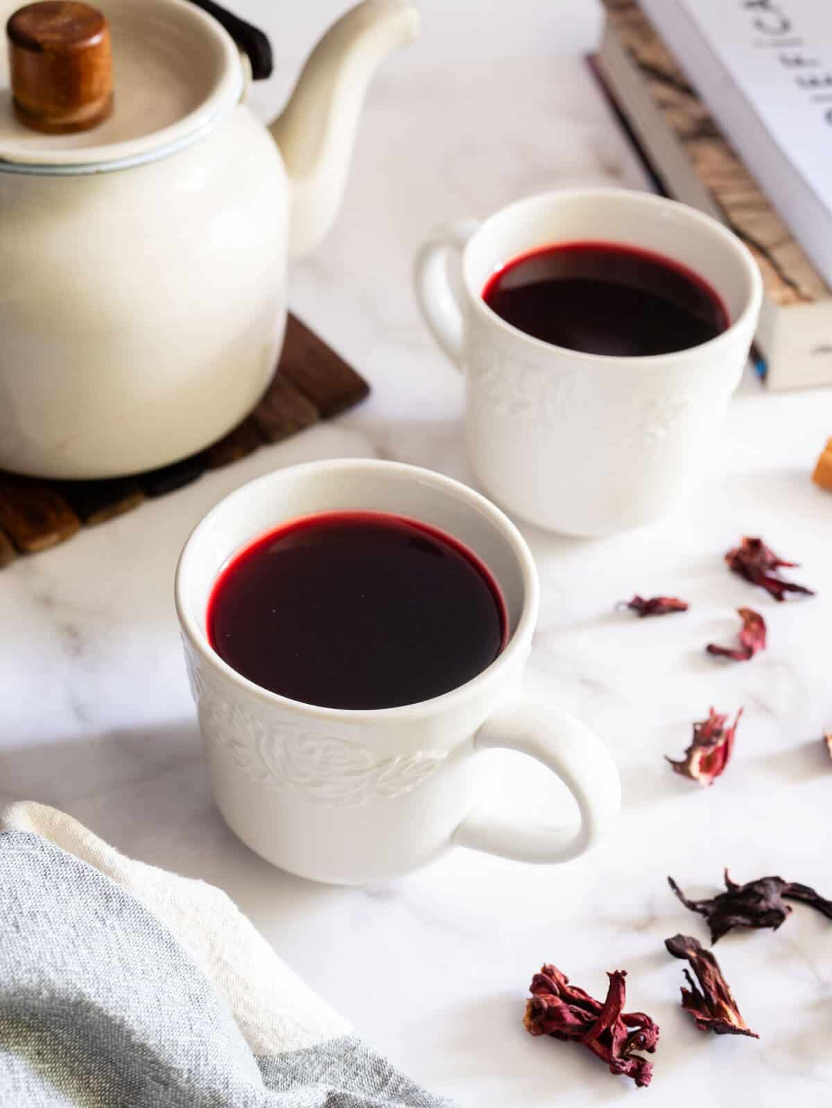 served hibiscus tea in white cups, next to an old kettle.