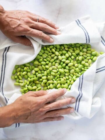 pat drying the edamame beans with a clean tea cloth.