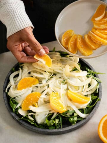 arranging orange slices on top of the salad.