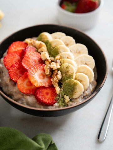 served oatmeal bowl with optional toppings: moringa powder, crushed almonds, sliced banana, and strawberries.