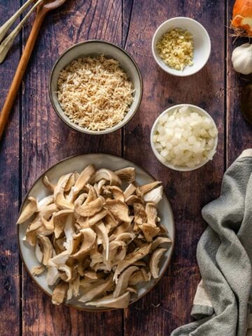 prepared ingredients in bowls: teared oyster mushrooms, shredded tofu, chopped onions, and garlic.