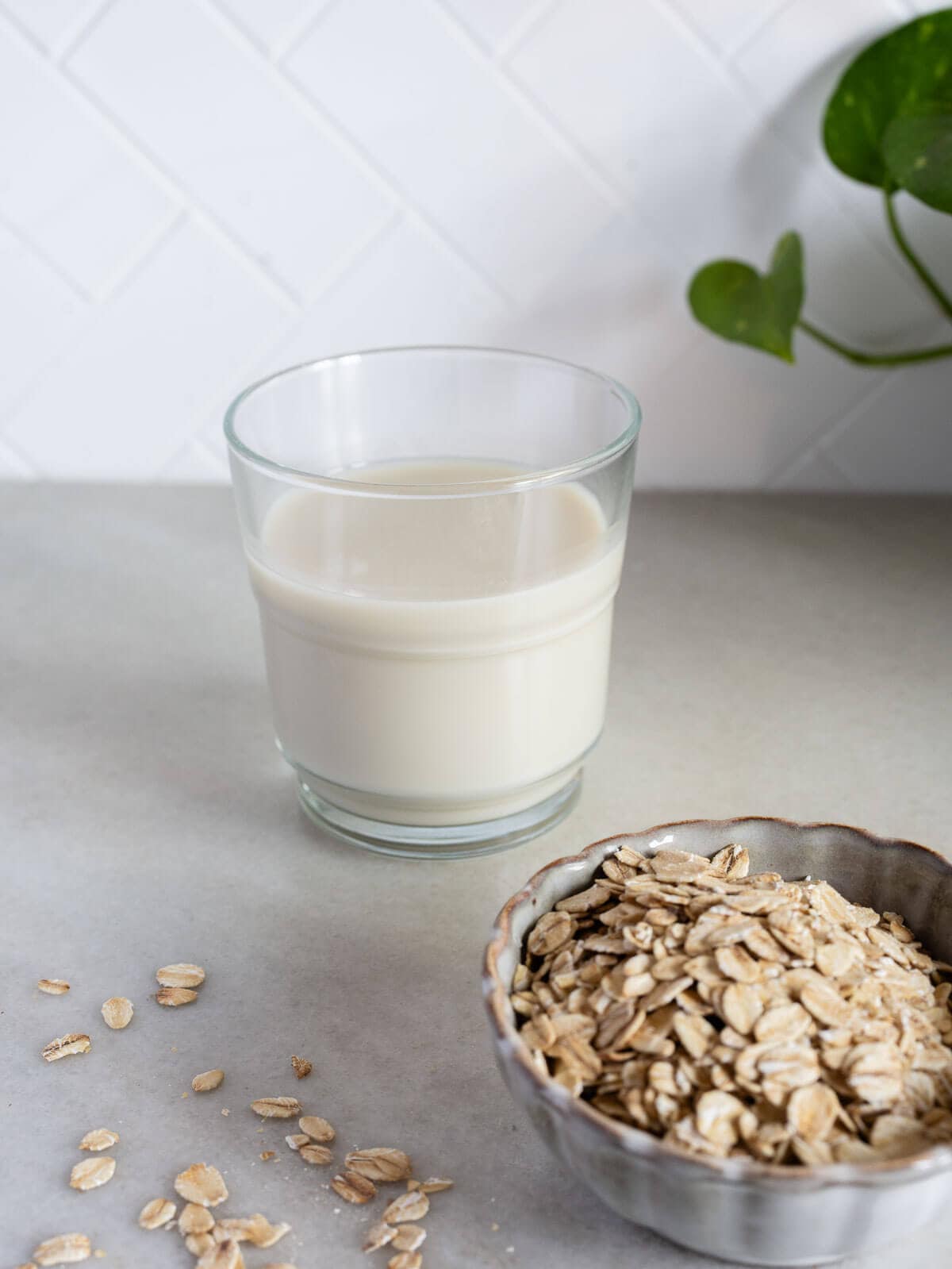 glass of oat milk next to rolled oats in a bowl.