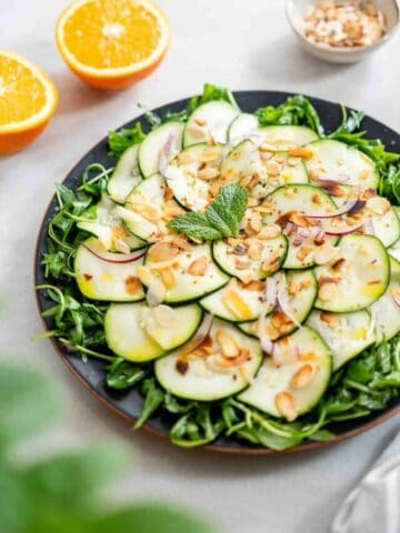 An inviting plate of marinated raw zucchini salad, elegantly presented with a garnish of herbs, ready to be served.