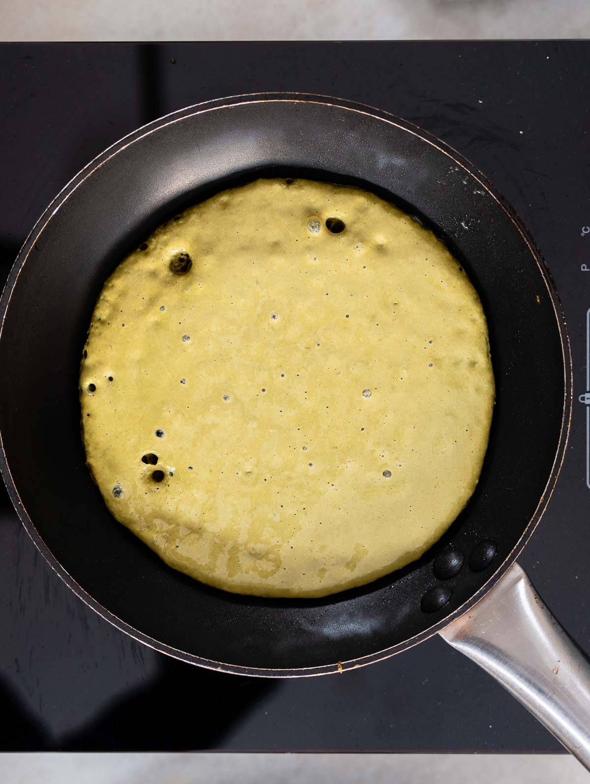 Matcha pancake batter in a skillet, with the first bubble popping on the surface.