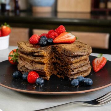 Ginger matcha pancakes topped with red berries, with a triangular section cut out to reveal the fluffy interior.