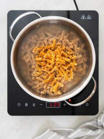 Chickpea pasta boils in a large pot filled with bubbling water,