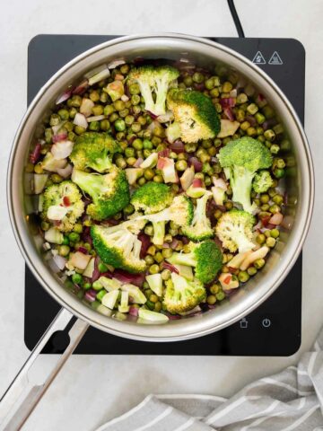 Pouring lemon juice into a hot pan to deglaze and lift the flavors from sautéed garlic, onions, green peas, and broccoli, creating a fragrant and colorful mixture.