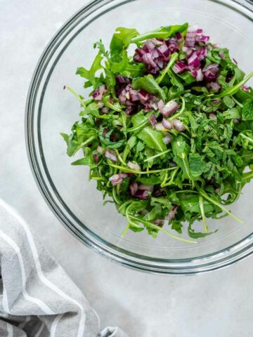 Fresh arugula and herbs mixed in a bowl, forming the leafy base of a flavorful marinated raw zucchini salad.