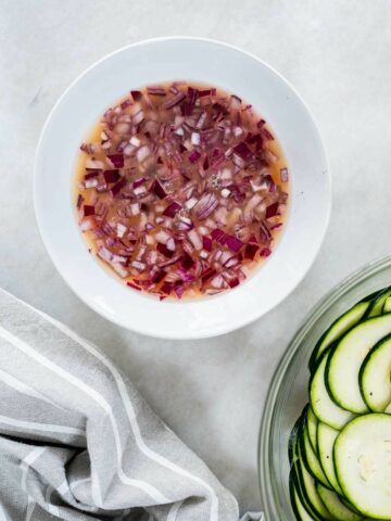 A bowl of finely chopped red onions sits next to a clear dressing, ingredients coming together for the salad.
