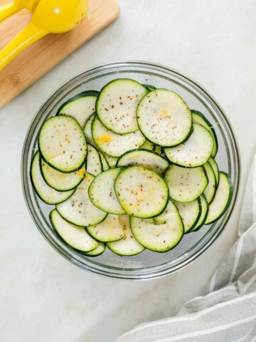 Sliced zucchini in a bowl seasoned with spices, ready for the flavors to meld.