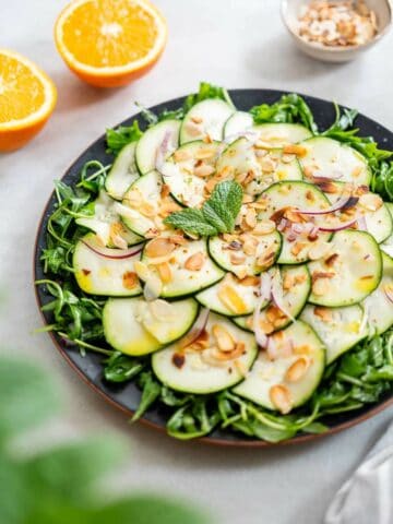An inviting plate of marinated raw zucchini salad, elegantly presented with a garnish of herbs, ready to be served.