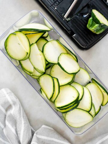 A mandolin container filled with perfectly sliced zucchini, prepped for marinating in a zesty dressing.